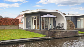 Moderno lodge al Water park De Bloemert 6 con terrazza, ombrellone, sedie e vista sul canale.