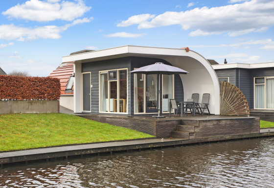 Moderno albergue en Water park De Bloemert 6 con terraza, sombrilla y vistas al canal desde la casa.