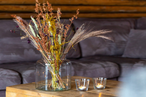 Bouquet di fiori secchi in vaso di vetro e due candele accese su un tavolo di legno davanti a un divano.