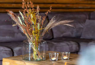 Bouquet di fiori secchi in vaso di vetro e due candele accese su un tavolo di legno davanti a un divano.