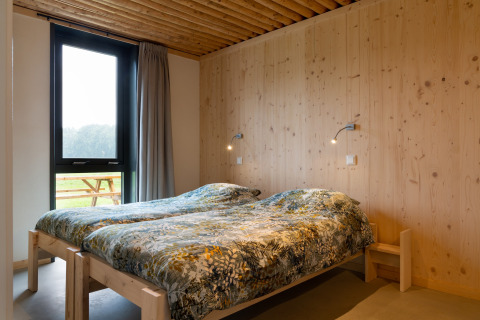 Slaapkamer met twee eenpersoonsbedden, houten muren en groot raam bij Koe in de Kost 4 lodge, Nederland.