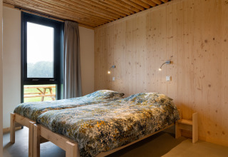 Slaapkamer met twee eenpersoonsbedden, houten muren en groot raam bij Koe in de Kost 4 lodge, Nederland.