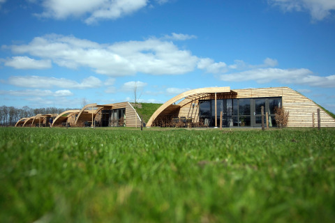 Duurzame houten lodges op groen veld onder blauwe lucht bij Koe in de Kost 4 in Nederland overdag.