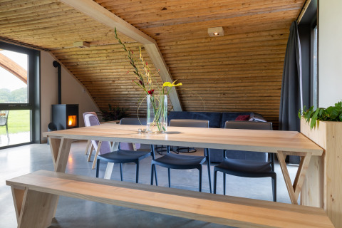 Moderne eethoek in lodge Koe in de Kost 4 in Nederland met houten tafel, bank en gezellige inrichting.