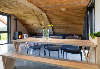 Moderne eethoek in lodge Koe in de Kost 4 in Nederland met houten tafel, bank en gezellige inrichting.