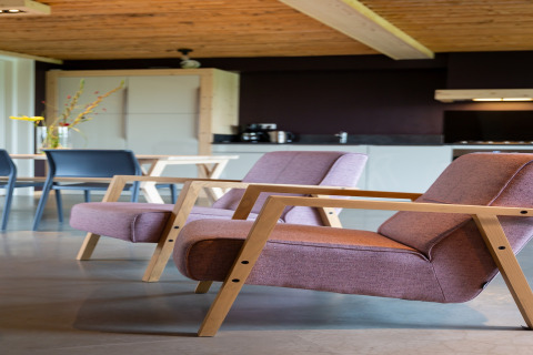 Moderne woonkamer met twee paarse stoelen, houten armleuningen, eettafel en keuken in een gezellig lodge.