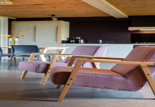 Moderne woonkamer met twee paarse stoelen, houten armleuningen, eettafel en keuken in een gezellig lodge.