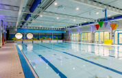 Indendørs swimmingpool med farverige spande, runde vinduer og vægmalerier af havliv.