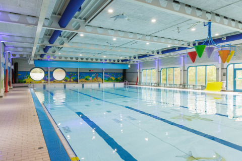Piscina al coperto con secchi colorati, finestre rotonde e murales acquatici sulle pareti.