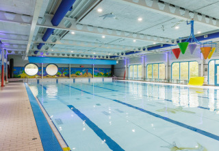 Piscina al coperto con secchi colorati, finestre rotonde e murales acquatici sulle pareti.