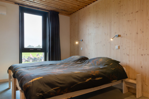 Slaapkamer met houten wanden, groot bed en raam in de lodge Koe in de Kost 4 in Nederland.