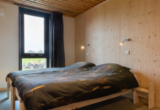 Slaapkamer met houten wanden, groot bed en raam in de lodge Koe in de Kost 4 in Nederland.