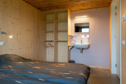 Knusse slaapkamer bij Koe in de Kost 4 in Nederland met houten wanden, open kast en een wastafel.
