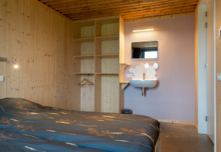 Knusse slaapkamer bij Koe in de Kost 4 in Nederland met houten wanden, open kast en een wastafel.