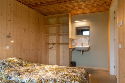 Slaapkamer met houten wanden, open kast en wastafel bij lodge Koe in de Kost 4 in Nederland.