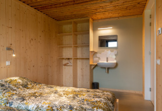 Slaapkamer met houten wanden, open kast en wastafel bij lodge Koe in de Kost 4 in Nederland.
