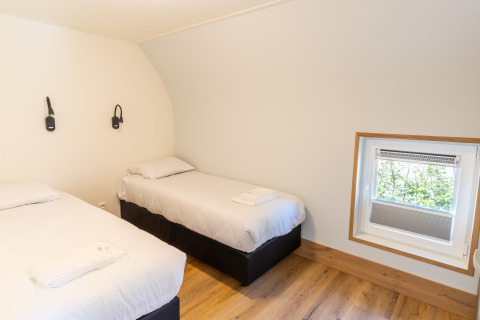 Twin bedroom with white linens, wood flooring, and a small window at 't Landgoed Baars 1 lodge, Netherlands.