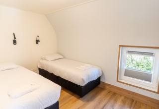 Twin bedroom with white linens, wood flooring, and a small window at 't Landgoed Baars 1 lodge, Netherlands.
