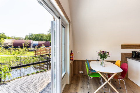 Interior of a lodge with colorful chairs, open doors, garden and water view at ’t Landgoed Baars 1 in Netherlands.