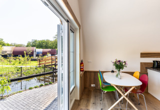 Interior of a lodge with colorful chairs, open doors, garden and water view at ’t Landgoed Baars 1 in Netherlands.