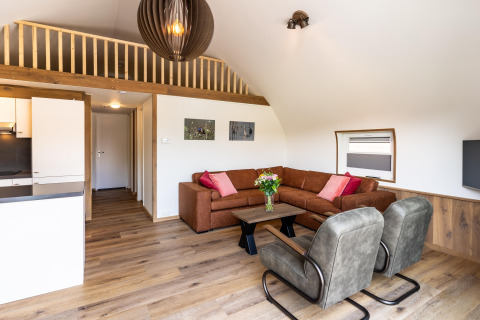Modern living room at lodge 't Landgoed Baars 1 with brown sofa, armchairs, and wood flooring, Netherlands.