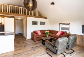 Modern living room at lodge 't Landgoed Baars 1 with brown sofa, armchairs, and wood flooring, Netherlands.
