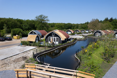 Charming cottages along a canal at 't Landgoed Baars 1 lodge in the Netherlands, surrounded by greenery.
