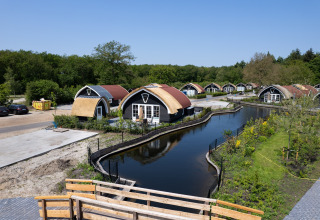 Charming cottages along a canal at 't Landgoed Baars 1 lodge in the Netherlands, surrounded by greenery.