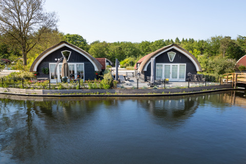 Two cozy lodges at 't Landgoed Baars 1 in the Netherlands, located by the water and lush greenery.