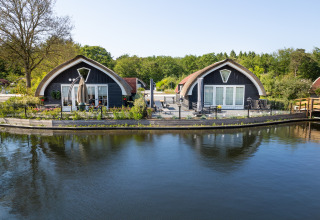 Two cozy lodges at 't Landgoed Baars 1 in the Netherlands, located by the water and lush greenery.