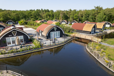 Curved-roof lodges by a canal and forest viewed from above at 't Landgoed Baars 1 in the Netherlands.