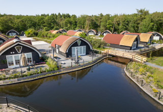 Curved-roof lodges by a canal and forest viewed from above at 't Landgoed Baars 1 in the Netherlands.