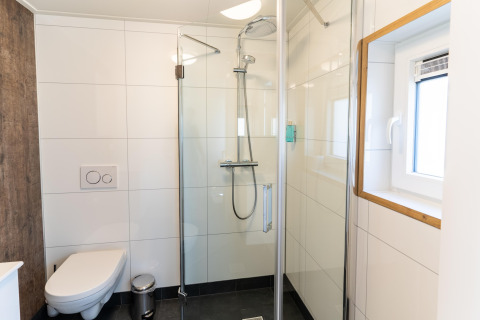 Modern bathroom with glass shower, wall-mounted toilet and window at ‘t Landgoed Baars 1 lodge in the Netherlands.