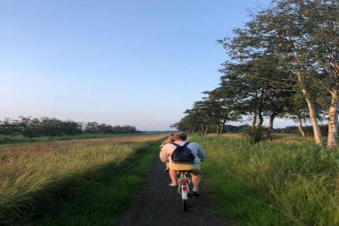 Two people cycling down a narrow path through green fields and trees at 't Landgoed Baars 1, Netherlands.