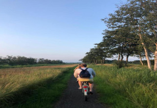 Two people cycling down a narrow path through green fields and trees at 't Landgoed Baars 1, Netherlands.