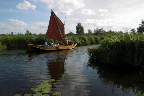 A group of people sailing in a traditional boat with red sail at 't Landgoed Baars 1 in the Netherlands.