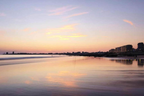 Sunset view from the beach at 't Landgoed Baars 1 lodge, showing city lights in the Netherlands.