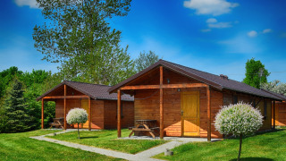 Houten chalets op Cottages Ranch by the Sea met groen gras, struiken en een stralend blauwe lucht erboven.