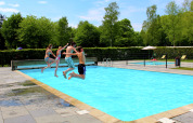 Vier Jugendliche springen gemeinsam in den Pool von Residence De Eese 3, umgeben von Natur.