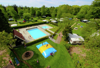 Luchtfoto van een glamping met zwembad, springkussen, caravans en groene zones omringd door bomen.