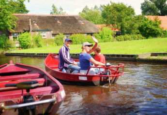 Drei Personen fahren in einem roten Boot auf einem Kanal vor der Lodge Residence De Eese 3 in den Niederlanden.