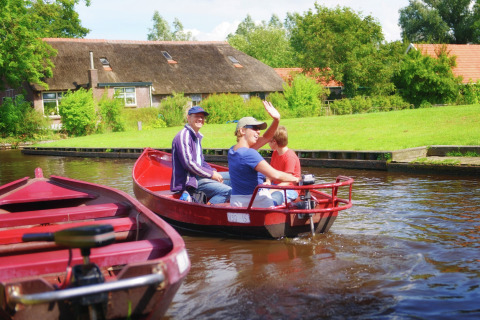 Drie mensen varen in een rode boot op een kanaal bij Residence De Eese 3 lodge in Nederland, omgeven door groen.