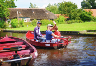 Drie mensen varen in een rode boot op een kanaal bij Residence De Eese 3 lodge in Nederland, omgeven door groen.