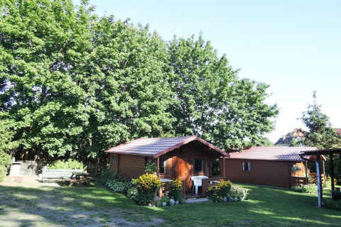 Accogliente bungalow in legno Bungalows Lubin Tipo A Jolanta, circondato da fiori e verde in una giornata soleggiata.