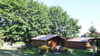Cozy wooden cabin Bungalows Lubin Type A Jolanta surrounded by flowers and greenery on a sunny day.