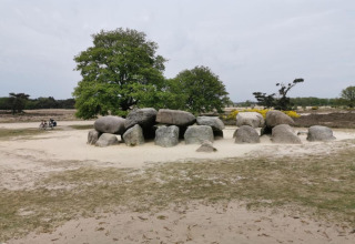 Foto van grote oude stenen in een cirkel op zandgrond bij bomen op een glampinglocatie.