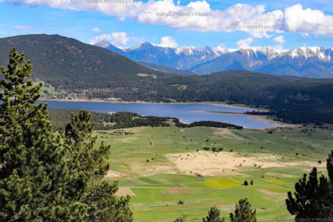 Panoramisch uitzicht op groene velden, een blauw meer en besneeuwde bergen onder een heldere lucht.