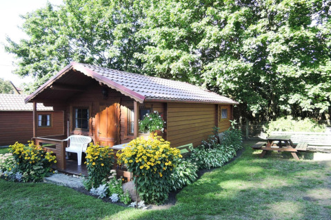 Photo d’un chalet en bois charmant, Bungalows Lubin-Type B (Henryk), entouré de fleurs et d’arbres verdoyants.