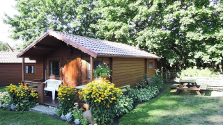 Photo of a cozy wooden cabin, Bungalows Lubin-Type B (Henryk), with flowers and a picnic bench in the garden.