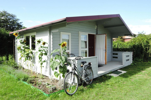 Pequeña cabaña gris con bicicleta al frente y girasoles en el jardín en At słonecznikiem, día soleado.